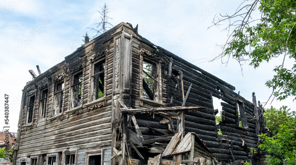 Burnt house on a city street in Russia. Wooden building after the fire. Remains of a residential building after a fire incident. Sunny day. Summer. Burnt house on a city street in Russia. Wooden building after the fire. Remains of a residential building after a fire incident. Sunny day. Summer.