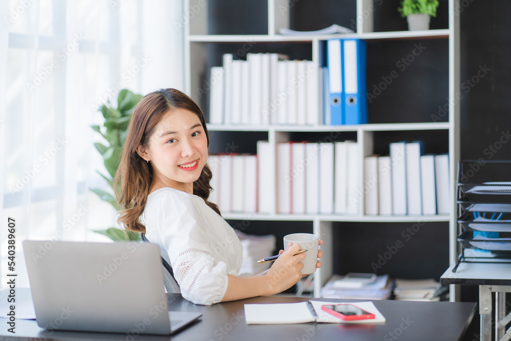Beautiful Asian businesswoman working on a desk with a laptop with a smiling face while looking at the document received in the office. Beautiful Asian businesswoman working on a desk with a laptop with a smiling face while looking at the document received in the office.