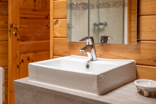 A white sink with a metal faucet in a cozy bathroom with wooden walls.