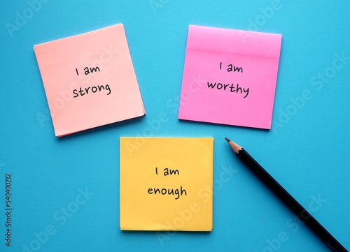 Three note paper on blue background with handwritten text I AM STRONG, I AM WORTHY, I AM ENOUGH - powerful self talk positive affirmations to boost self confidence in daily life photo
