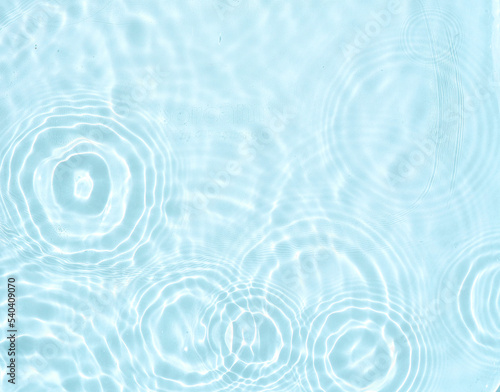 Original beautiful background image in a light blue hue for creative work or design in form of a water surface with chaotic circular waves and a play of light and shadow.