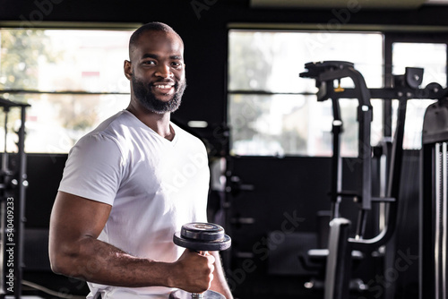 Fit and muscular african man doing biceps workouts with dumbbells in gym, copy space.