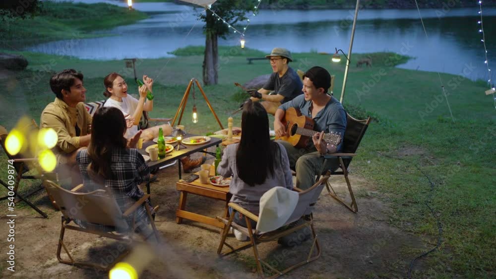 Group of Happy Asian people enjoy and fun outdoor lifestyle camping together on holiday travel vacation. Man and woman friends playing guitar and singing together while having dinner at summer night. Group of Happy Asian people enjoy and fun outdoor lifestyle camping together on holiday travel vacation. Man and woman friends playing guitar and singing together while having dinner at summer night.