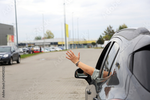 Dłoń kobiety, ręka wysunięta przez okno samochodu osobowego, suwa, na placu przed marketem.