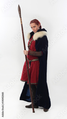 full length portrait of beautiful woman wearing a red medieval fantasy warrior costume with leather armour, holding weapons. Standing pose isolated on white studio background.