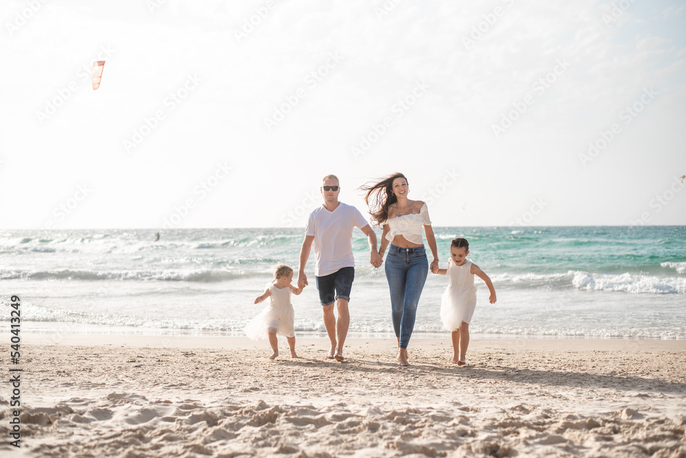 Happy family: parents and two daughters walking on beach in summer vacation. Run, play and get fun on sand near sea together. white clothes and jeans. 