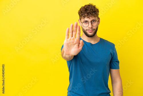 Young handsome caucasian man isolated on yellow background making stop gesture © luismolinero