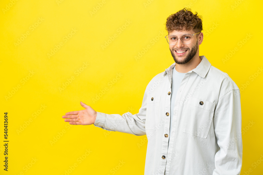 Young handsome caucasian man isolated on yellow background extending hands to the side for inviting to come Young handsome caucasian man isolated on yellow background extending hands to the side for inviting to come