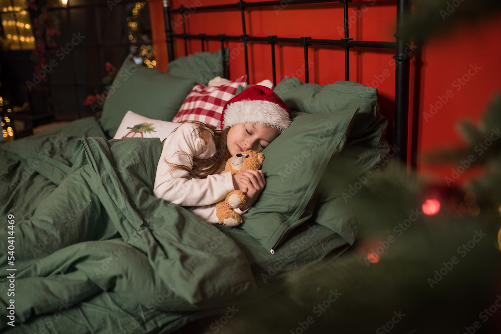 a little girl in a santa hat sleeps on a green bedding in her bedroom for christmas, christmas magic, a tired child sleeps after celebrating new year or christmas