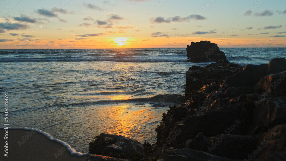 Beautiful natural landscape with sandy beach with big stones during sunset. Sun over horizon and Rolling ocean waves to the rocky shore while sunset. Summer tourist destination in Portugal. Travel Beautiful natural landscape with sandy beach with big stones during sunset. Sun over horizon and Rolling ocean waves to the rocky shore while sunset. Summer tourist destination in Portugal. Travel
