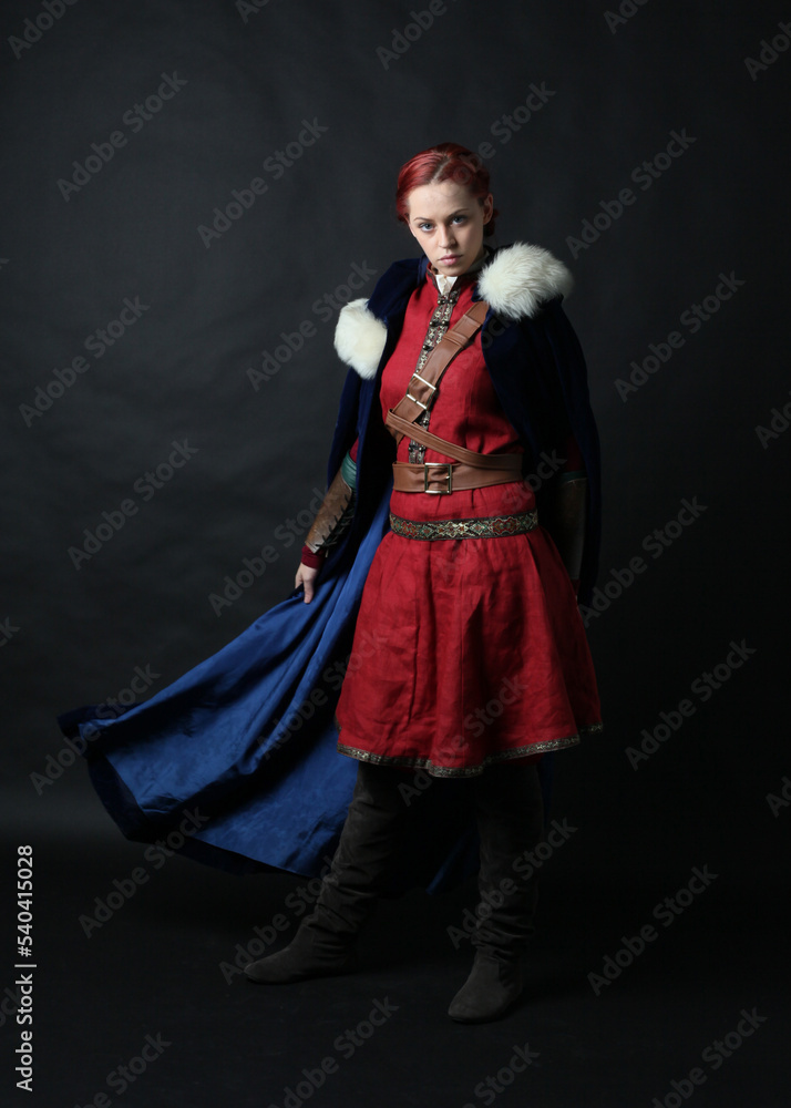  portrait of beautiful woman wearing a red medieval fantasy warrior costume with leather armour.  Standing pose isolated on studio background.