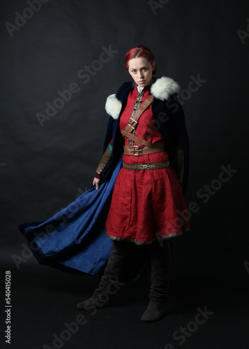  portrait of beautiful woman wearing a red medieval fantasy warrior costume with leather armour. Standing pose isolated on studio background.