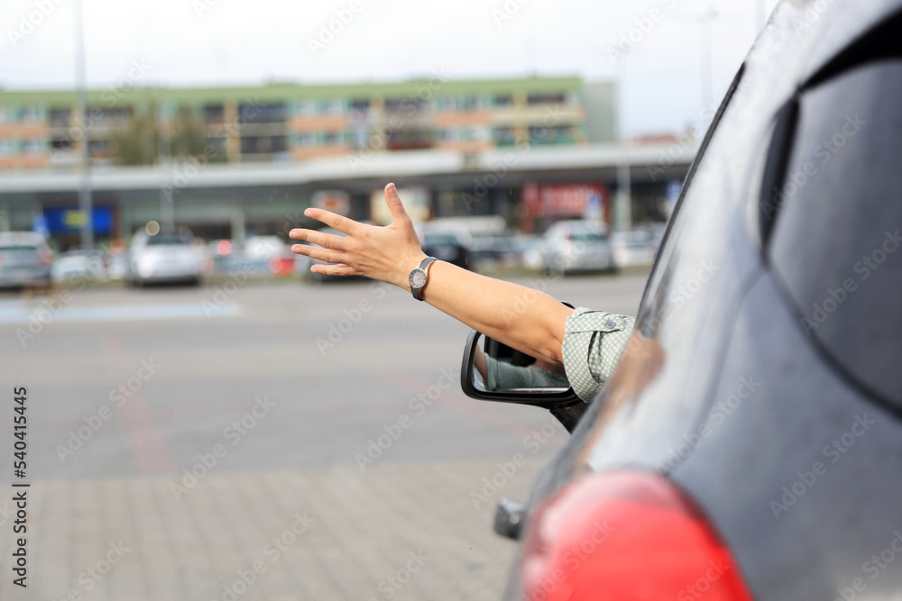 Dłoń kobiety, ręka wysunięta przez okno samochodu osobowego, suwa, na placu przed marketem. - obrazy, fototapety, plakaty 