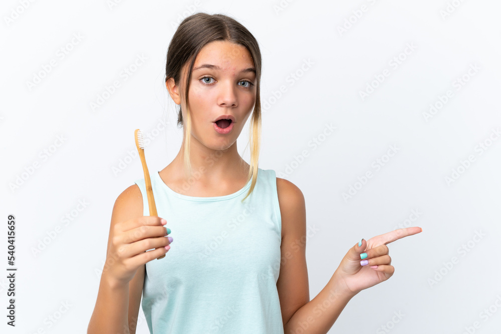 Little caucasian girl holding a toothbrush isolated on white background surprised and pointing side Little caucasian girl holding a toothbrush isolated on white background surprised and pointing side