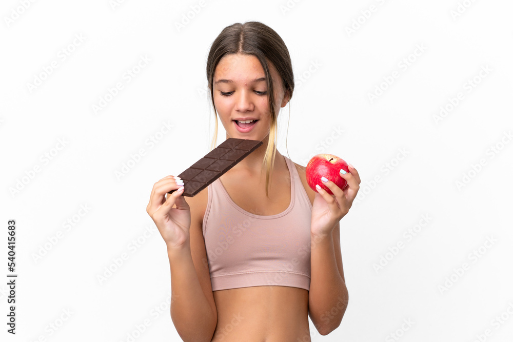 Little caucasian girl isolated on white background taking a chocolate tablet in one hand and an apple in the other Little caucasian girl isolated on white background taking a chocolate tablet in one hand and an apple in the other