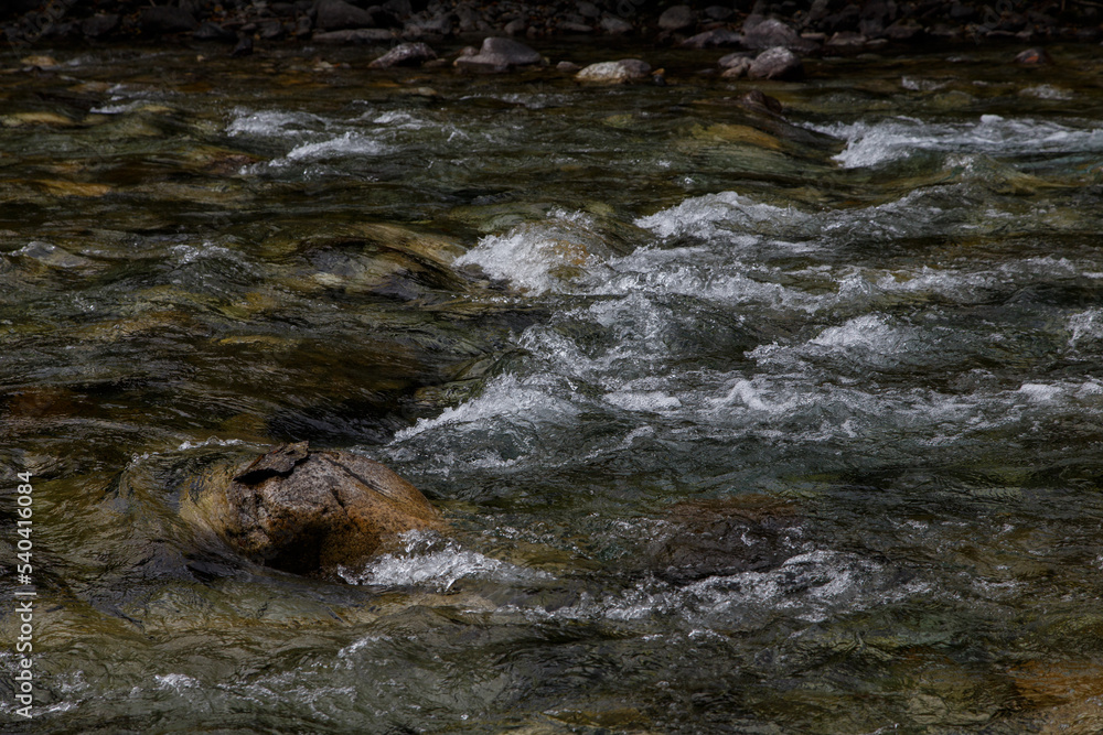 a large stone lies in the middle of a clear mountain river. The river bends around the stones creating river foam a large stone lies in the middle of a clear mountain river. The river bends around the stones creating river foam