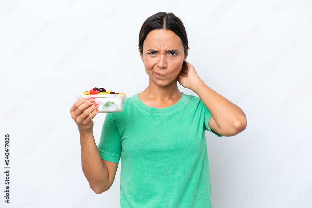 Young hispanic woman holding a bowl of fruit isolated on white background having doubts