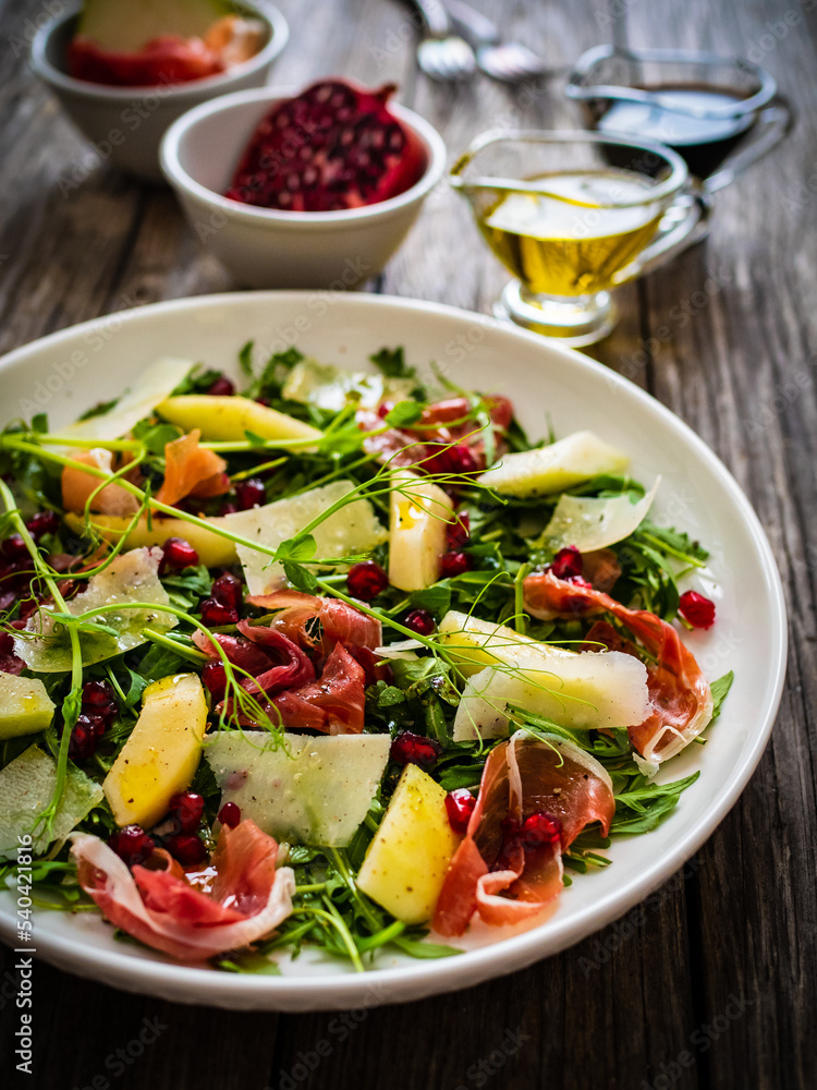 Fresh salad - prosciutto di Parma, pomegranate, pear, leafy vegetables and parmesan on wooden background
