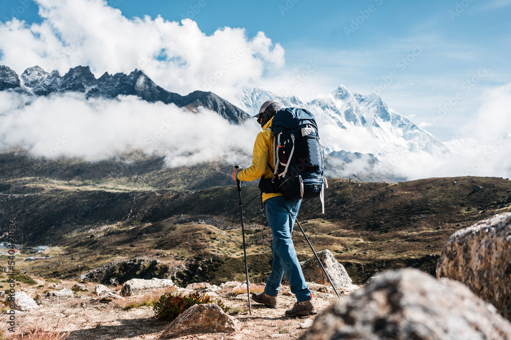 Solo hiker wearing professional and trekking poles walk across sunny mountain track. Young tourist traveling along rocky trek - obrazy, fototapety, plakaty 