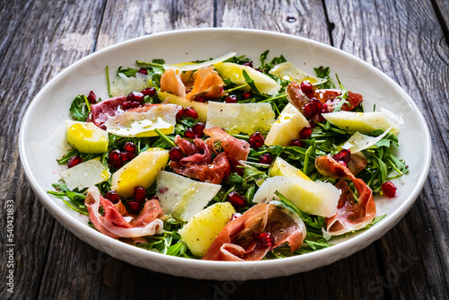Fresh salad - prosciutto di Parma, pomegranate, pear, leafy vegetables and parmesan on wooden background 