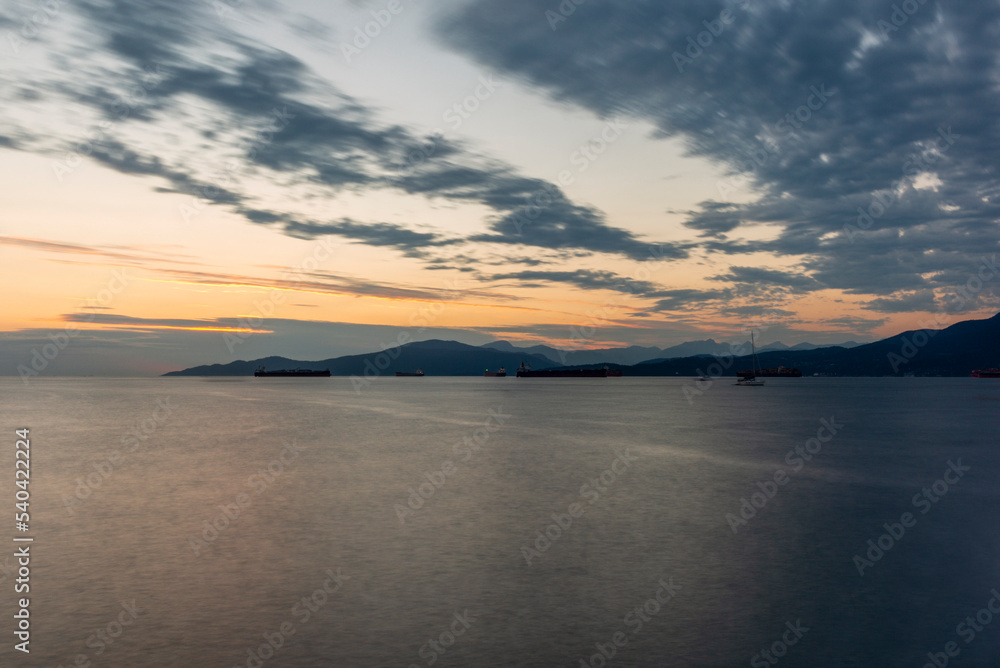Sunset on the sea in front of Vancouver with container ships, sail boat and stand-up paddles
