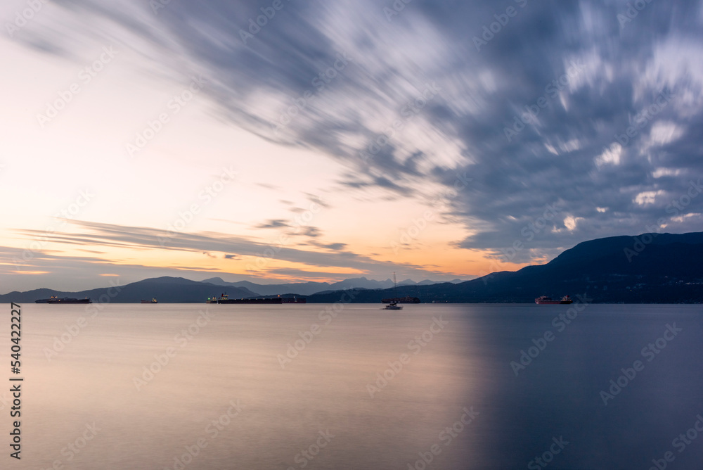Sunset on the sea in front of Vancouver with container ships, sail boat and stand-up paddles
