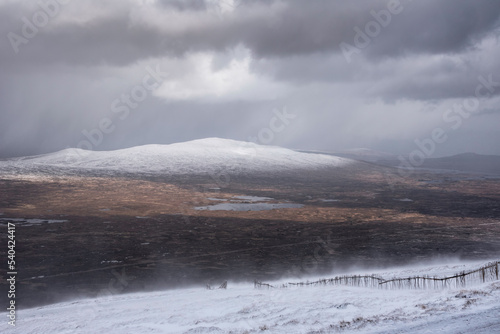 Epic Winter landscape image from mountain top in Scottish Highlands down towards Rannoch Moor during snow storm and spindrift off mountain top in high winds