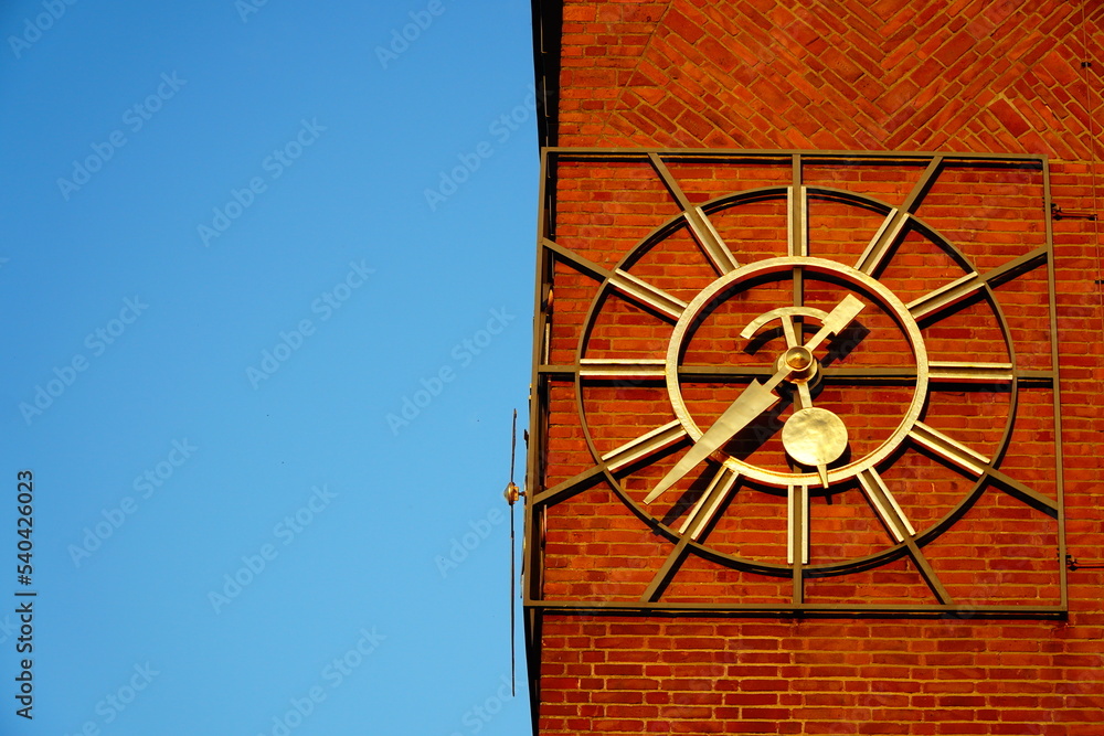 Obraz premium Golden clock on a brick building with a blue sky on the left