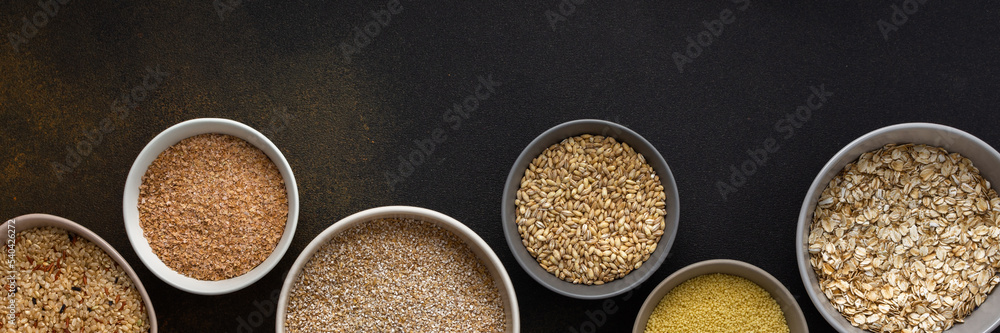 Various grain cereals in bowls banner, top view on a brown background with bowls of cereals