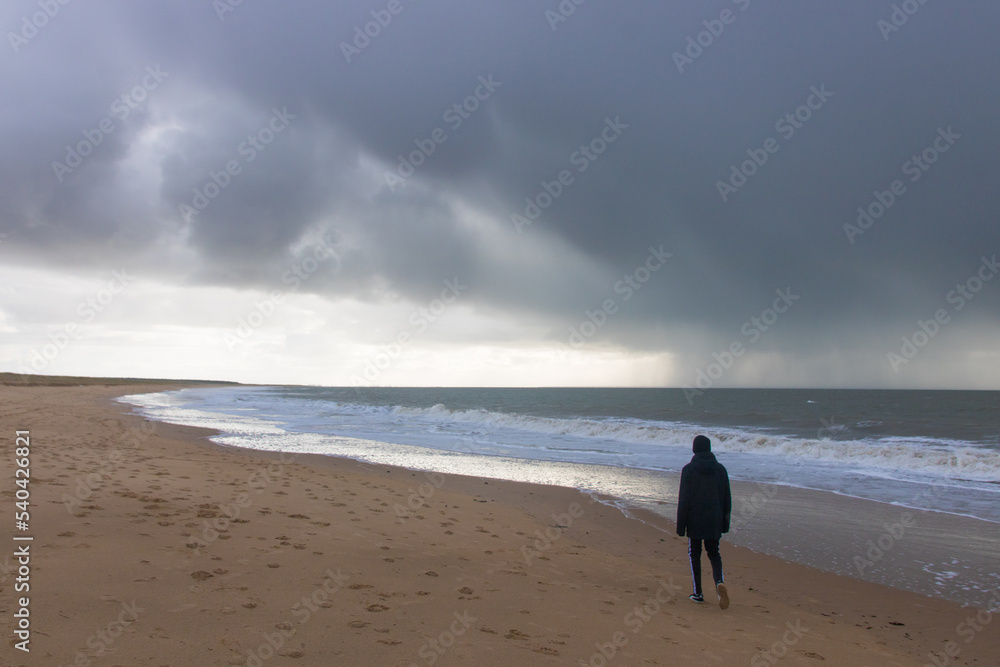 silhouette d'un jeune homme sur la plage sous un ciel orageux