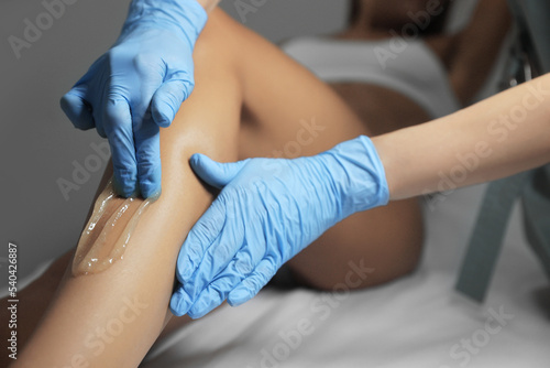 Young woman undergoing hair removal procedure on legs with sugaring paste in salon, closeup