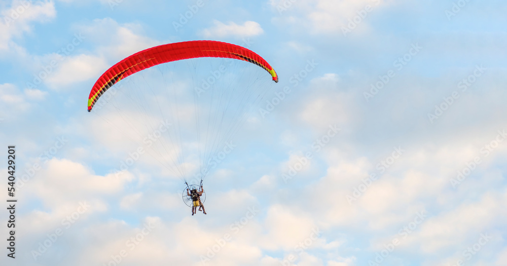 Against background of blue summer cloudy sky, tandem of paragliders flies on red ultralight aircraft - paraglider. Extreme sport and recreation. Against background of blue summer cloudy sky, tandem of paragliders flies on red ultralight aircraft - paraglider. Extreme sport and recreation.