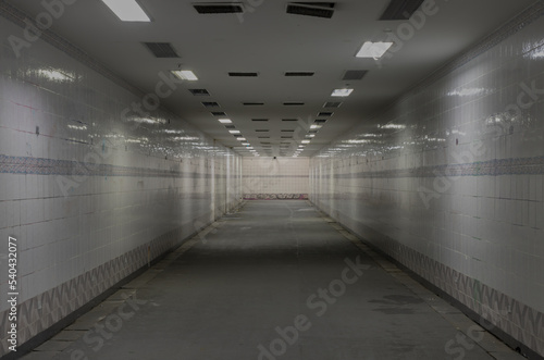 Perspective view of Ambient public underpass with white tiled walls and stripes of ceiling neon lights. Long pedestrian luminous tunnel, Space for text, Selective focus.