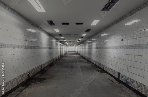 Perspective view of Ambient public underpass with white tiled walls and stripes of ceiling neon lights. Long pedestrian luminous tunnel, Space for text, Selective focus.