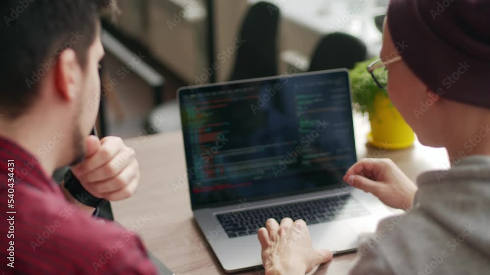 Two hipster coworkers sharing ideas about project sitting with laptops in spacious open space office. Developers discuss application program code. Coder and manager consulting software architecture.