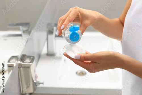 Woman pouring micellar water onto cotton pad in bathroom, closeup