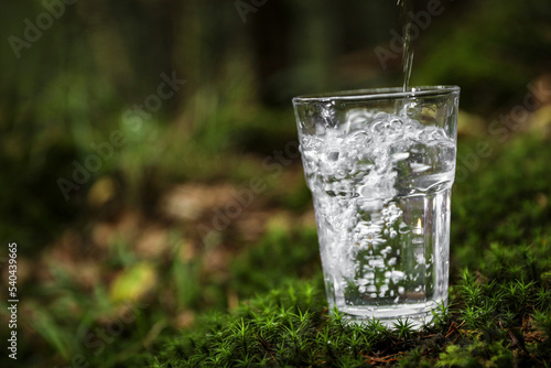 Pouring water into glass on green grass outdoors. Space for text