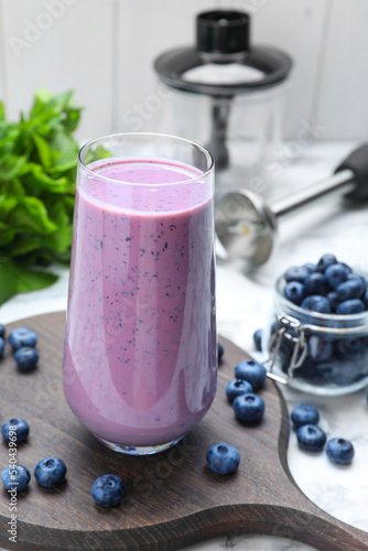 Glass of blueberry smoothie and fresh berries on white marble table