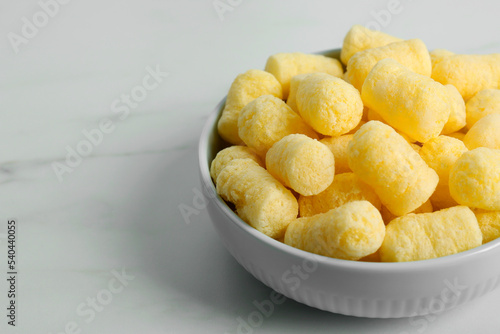 Bowl of delicious crispy corn sticks on white marble table. Space for text