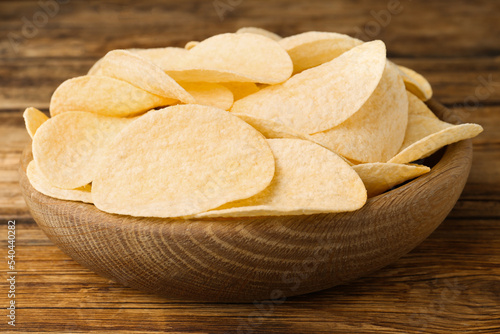 Bowl with delicious potato chips on wooden table, closeup