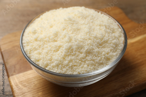Glass bowl with grated parmesan cheese on wooden table, closeup