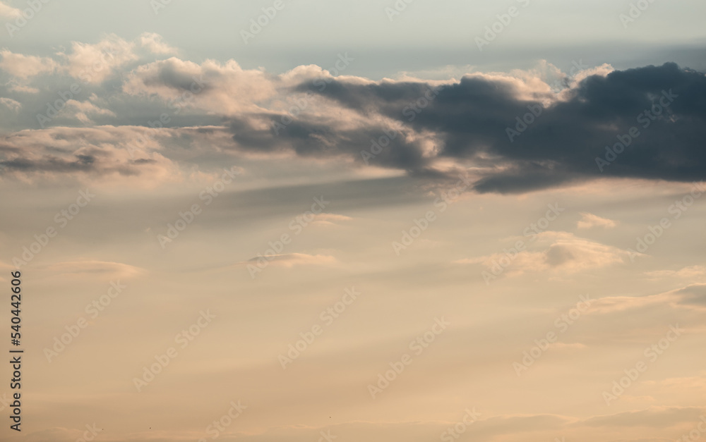 A sky with clouds obscuring the sun as it approaches the horizon. Clouds in yellow sunset light.