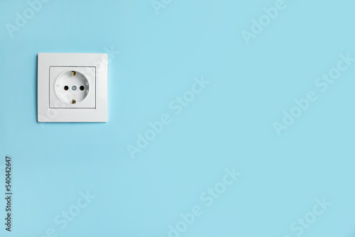 Power socket on light blue wall, space for text. Electrical supply