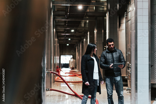 Caucasian couple during the winery visit, walking through the production industry cellar using a tablet to know the process of the winemaking