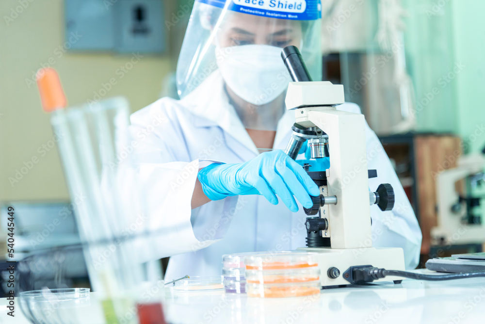 Woman scientist hand write note information in medical lab look at science microscope medical test, research biology chemistry. Asian Females technician laboratory analyzing blood test pharmaceutical Woman scientist hand write note information in medical lab look at science microscope medical test, research biology chemistry. Asian Females technician laboratory analyzing blood test pharmaceutical
