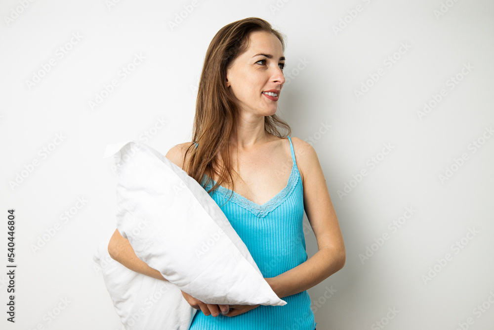 Young woman looking away holding white pillow on white background Young woman looking away holding white pillow on white background