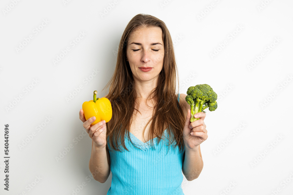 Fototapeta premium Young woman with closed eyes holding broccoli and paprika on white background