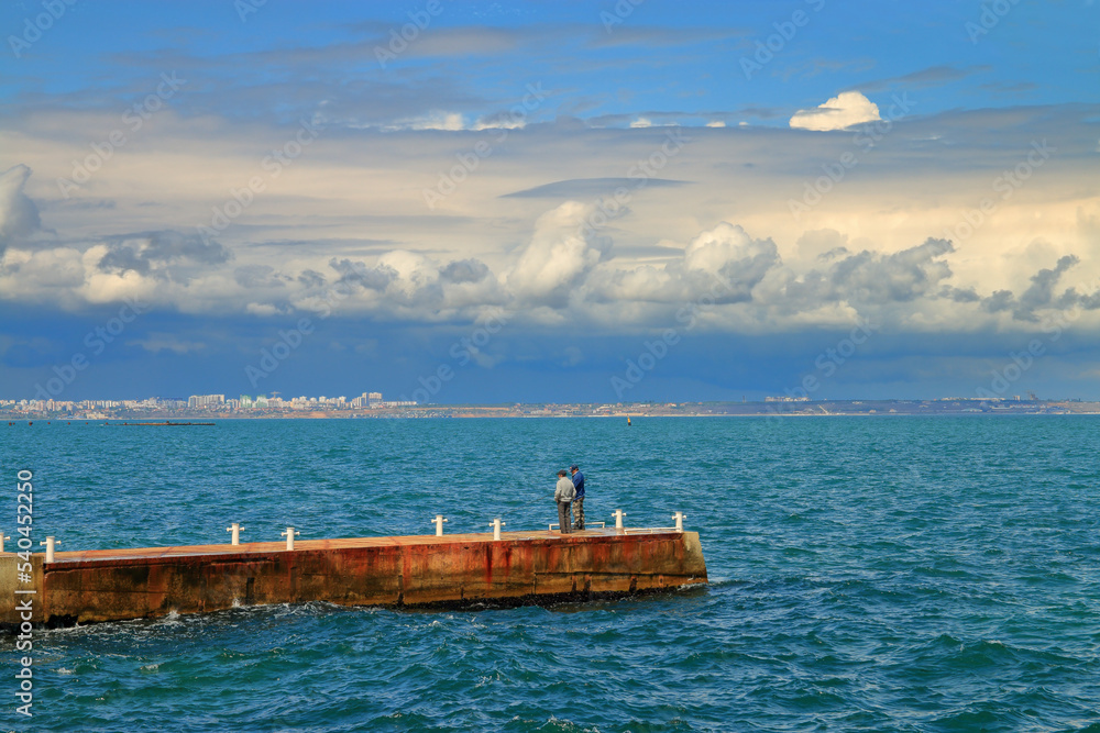 Sea cloudy landscape with a pier and fishermen.