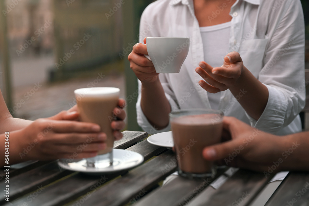 Friends drinking coffee and cocoa at wooden table in outdoor cafe, closeup Friends drinking coffee and cocoa at wooden table in outdoor cafe, closeup
