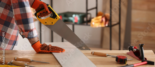 Carpenter sawing wooden plank at table in workshop, closeup. Banner design photo